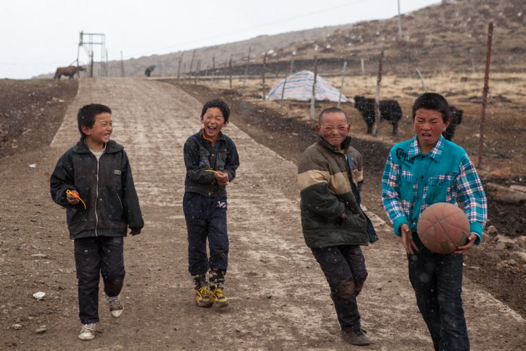 Vier Jungen kommen von einem Fussballspiel auf einer Dorfstraße entlang. Es hat gerade angefangen zu schneien. Langmusi - Gansu - China