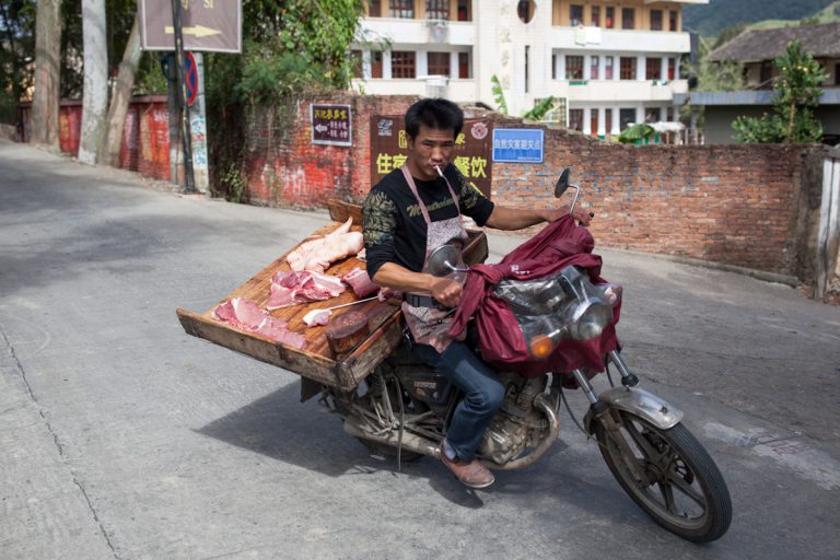 Ein Mann fährt vom Stand einer Fleischerei an einer Straße im Dorf weg, die er gerade beliefert hat. Yunshuiyao - Fujian - China