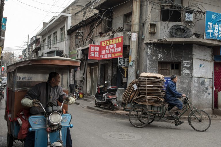 Ein Mann schaut einem anderen Mann nach, der mit seinem Dreirad gebrauchte Kartons sammelt. Xian - Shaanxi - China