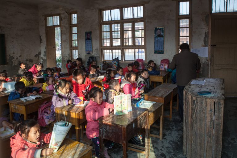 Ein Lehrer unterrichtet eine Schulklasse in einem Dorf auf dem Land. Jeder Schüler hat einen kleinen Tisch für sich, die eng aneinander stehen. Chengyang - Guangxi - China