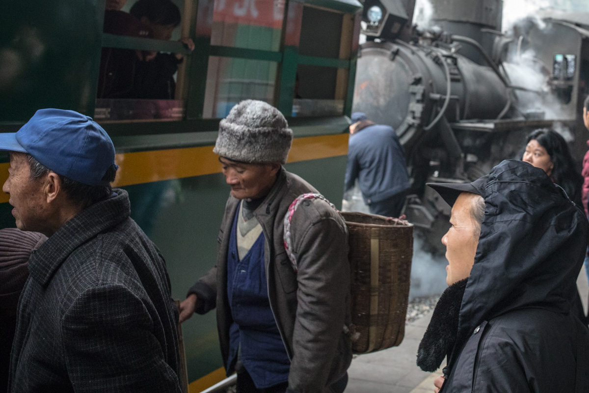 Mitfahrende steigen in Yejin in den Personenwaggon, während ein Eisenbahner die Dampflok ankoppelt. Yuejin Bagou - Sichuan - China