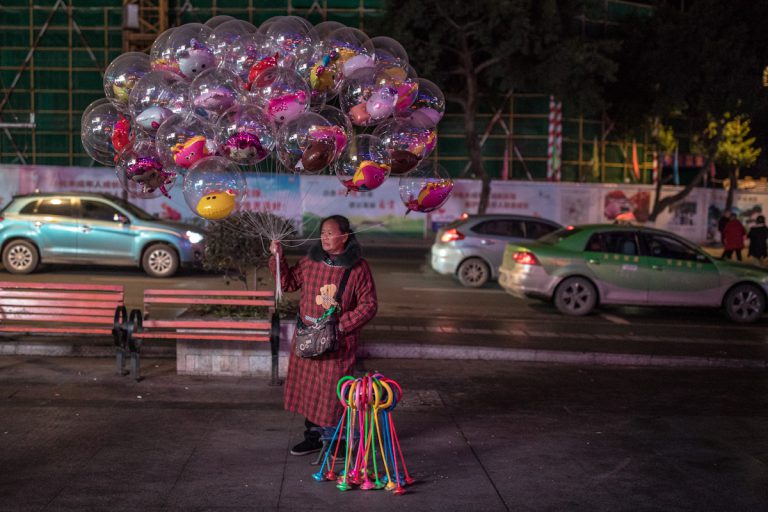 Eine Frau verkauft abends auf der Straße transparente Luftballons, die Innen verschiedene bunte aufgeblasenen Figuren beinhalten. Zigong - Sichuan - China