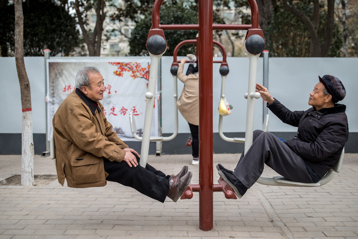 Zwei Pensionäre unterhalten sich beim Frühsport im Lianhu Park. Die Frau am Sportgerät dahinter, hebt ihre Beine bis zur oberen Stange. Xian - Shaanxi - China