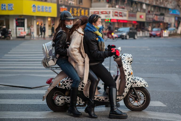 Drei Frauen sind gemeinsam auf einem bunten Mofa unterwegs. Warm angezogen warten sie gerade an einer Kreuzung. Hangzhou -Zhejiang - China
