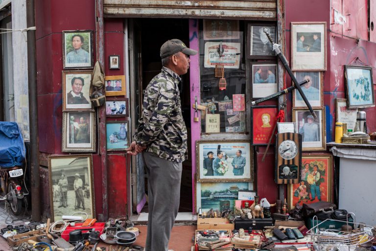 Ein Verkäufer steht vor seinem Geschäft mit Antiquitäten, wovon ein größerer Teil gerahmte Bilder mit Motiven von Mao Zedong einnimmt. Harbin - Heilongjiang - China