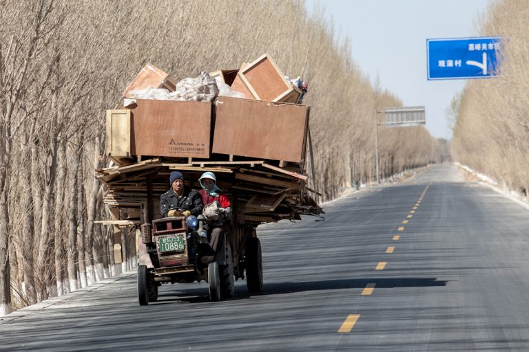 Eine Familie fährt mit ihrem Traktor und vollbeladenem Anhänger, der nach allen Seiten übersteht, auf der Landstraße nach Xinchengzhen. Das Dorf liegt in der Umgebung von Jiayuguan, im Nordwesten Chinas. Xinchengzhen - Gansu - China