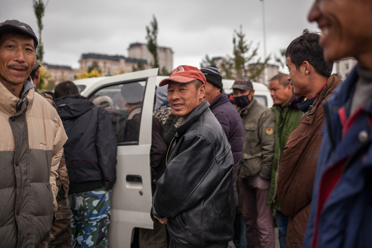 Die Männer sprechen mit einem anderen Mann in einem Auto, der Arbeiter für eine Tagesarbeit sucht. Hulun Buir - Innere Mongolei - China