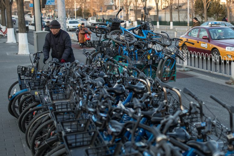 Ein Mitarbeiter eines Fahrradverleihers lädt Fahrräder auf einen Anhänger, an dem zu viele davon stehen. Peking - China