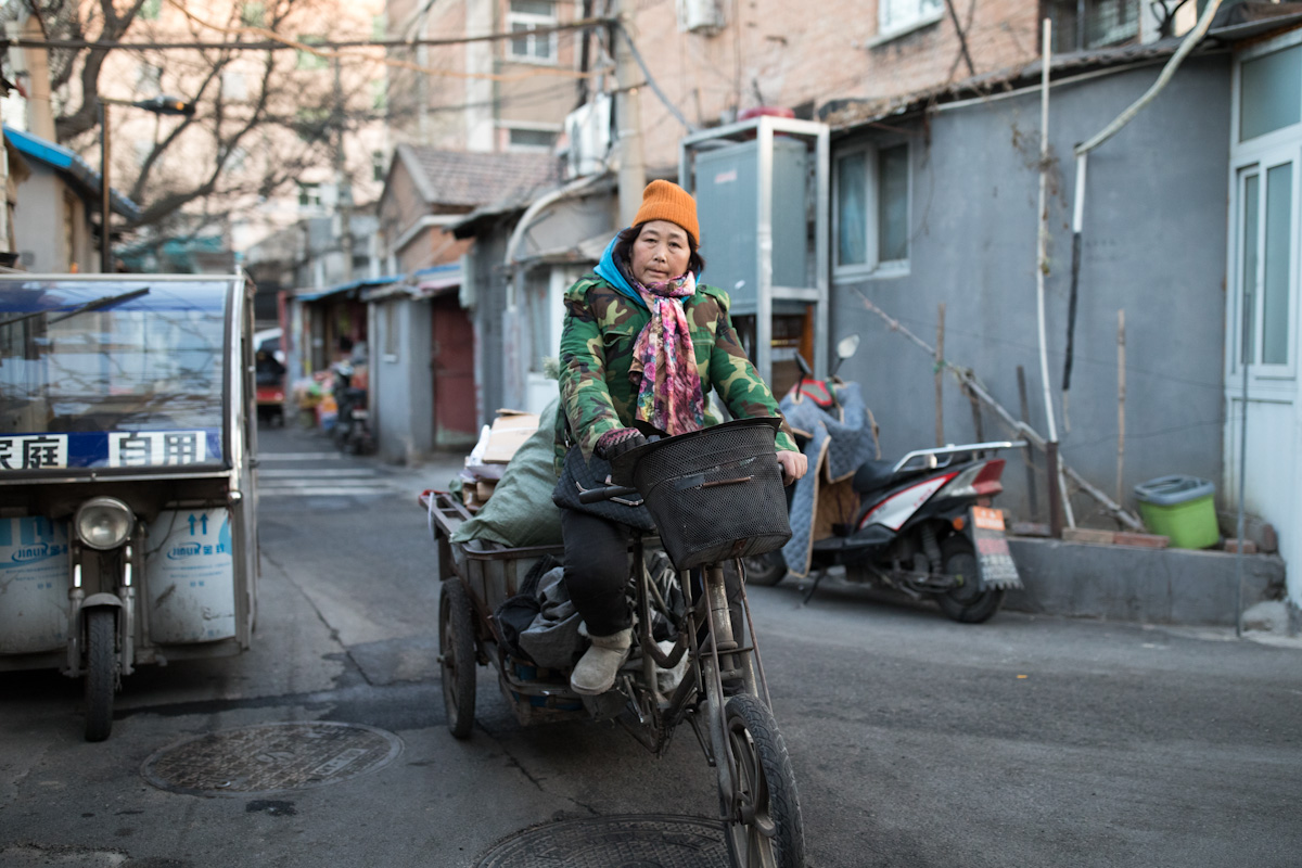 Eine Frau fährt mit ihrem beladenen Dreirad eine Straße in einem Hutong entlang. Peking - China